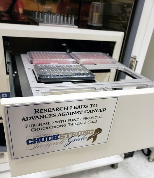 Cancer research laboratory equipment with a sign reading “Research Leads to Advances Against Cancer. Purchased with funds from the Chuckstrong Tailgate Gala.”